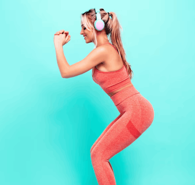 Woman in a coral sports set squatting against a turquoise wall
