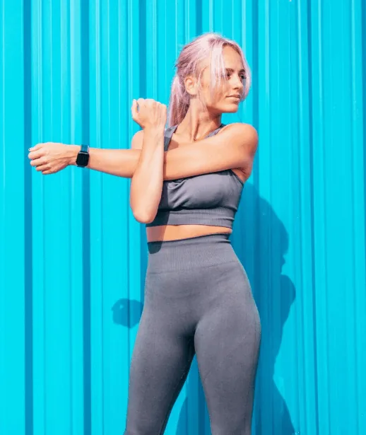 Woman in grey leggings stretching her arm against a blue backdrop