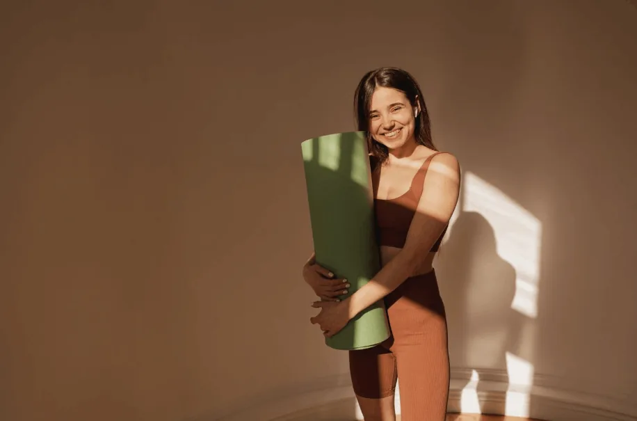 Smiling woman holding a rolled green yoga mat